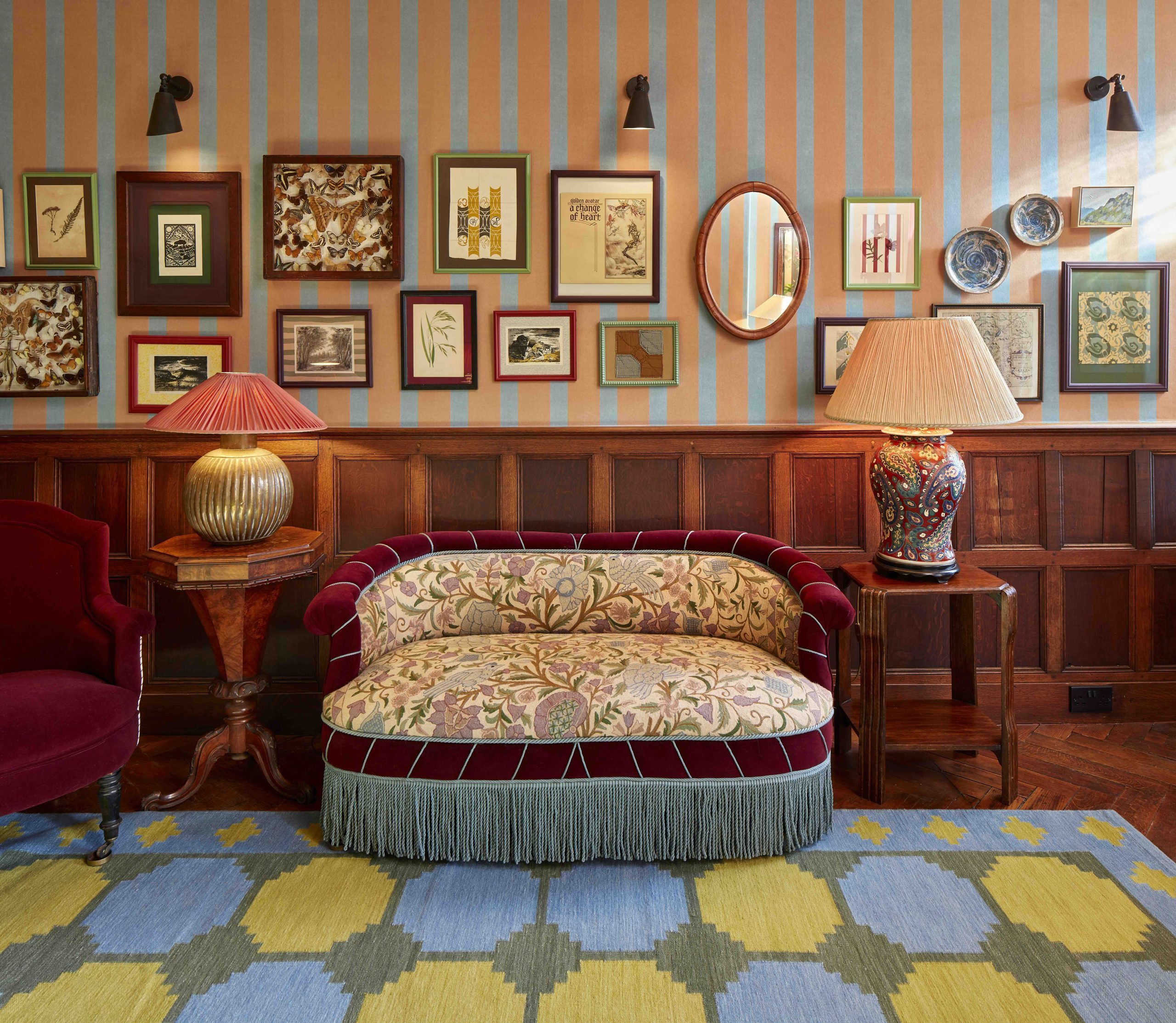 Stylish hotel interior with panelling, striped wallpaper, picture frames and fringed sofa